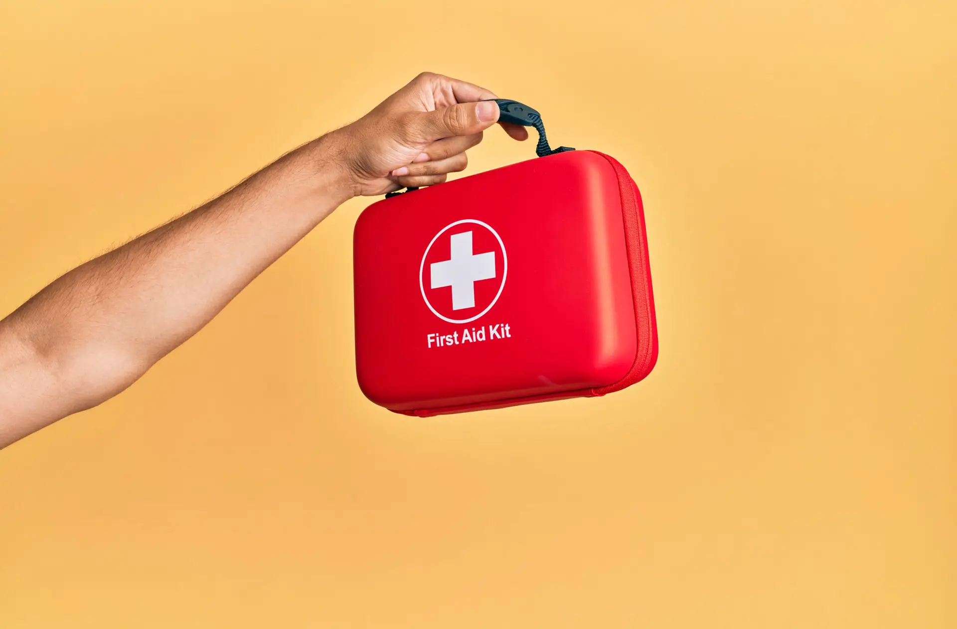 Hand of hispanic man holding first aid kit over isolated yellow background